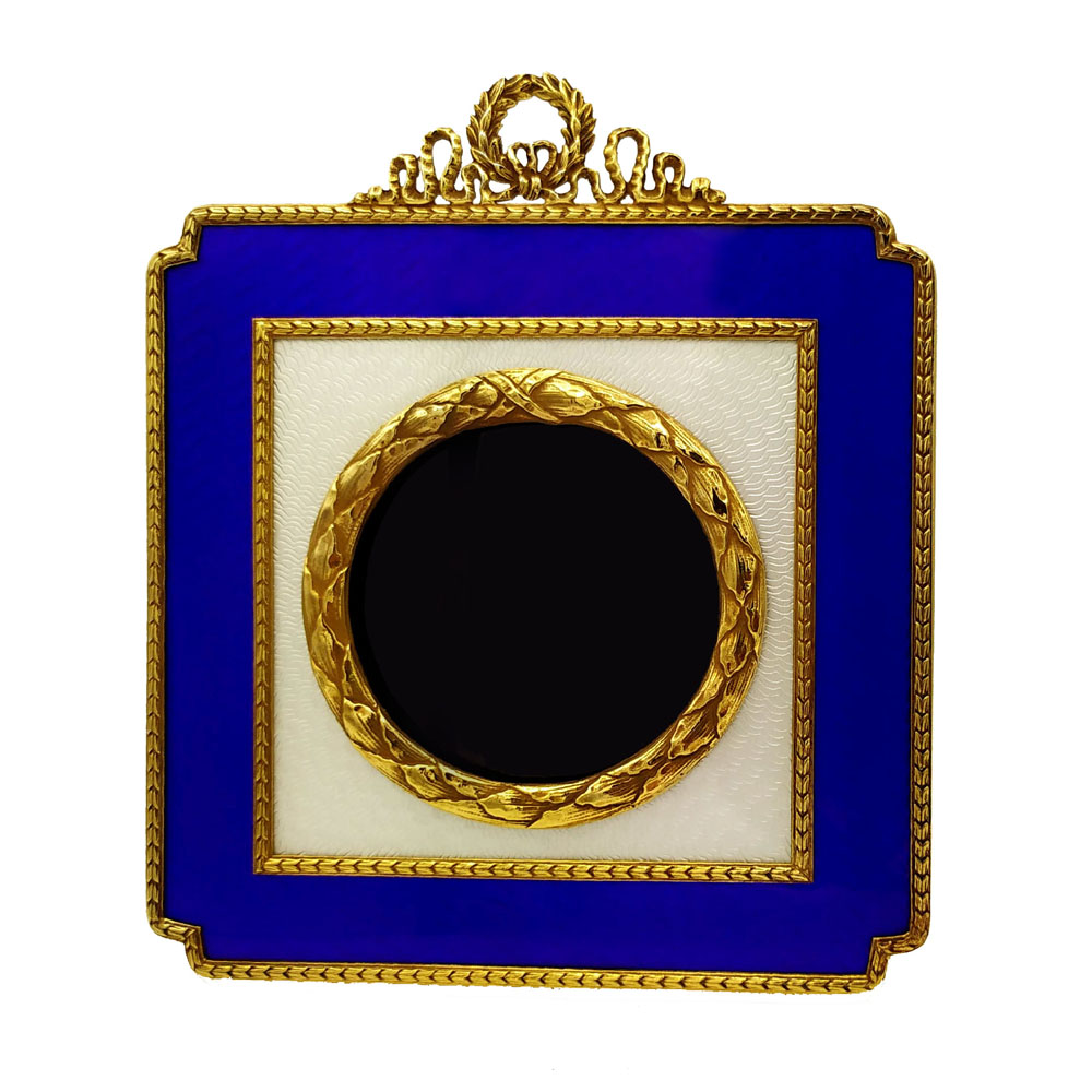 1892-6795 - Square table frame for round photos diameter cm. 7, in 925/1000 sterling silver gold plated with translucent two-tone fired enamels on guillochè, with borders and ornaments in the French Empire Napoleon III style. External cm. 14.5 x 14.5. Weight gr. 390. Designed by Giorgio Salimbeni in 1976 on inspiration from previous artefacts from the early 1900s and manufactured in Florence at the Salimbeni company headquarters in several specimens also with different colors, with completely manual execution by artisan artists with thick slab and large reinforcements suitable for sustaining numerous high-fire enamelled firings at approximately 750 < 800° C.