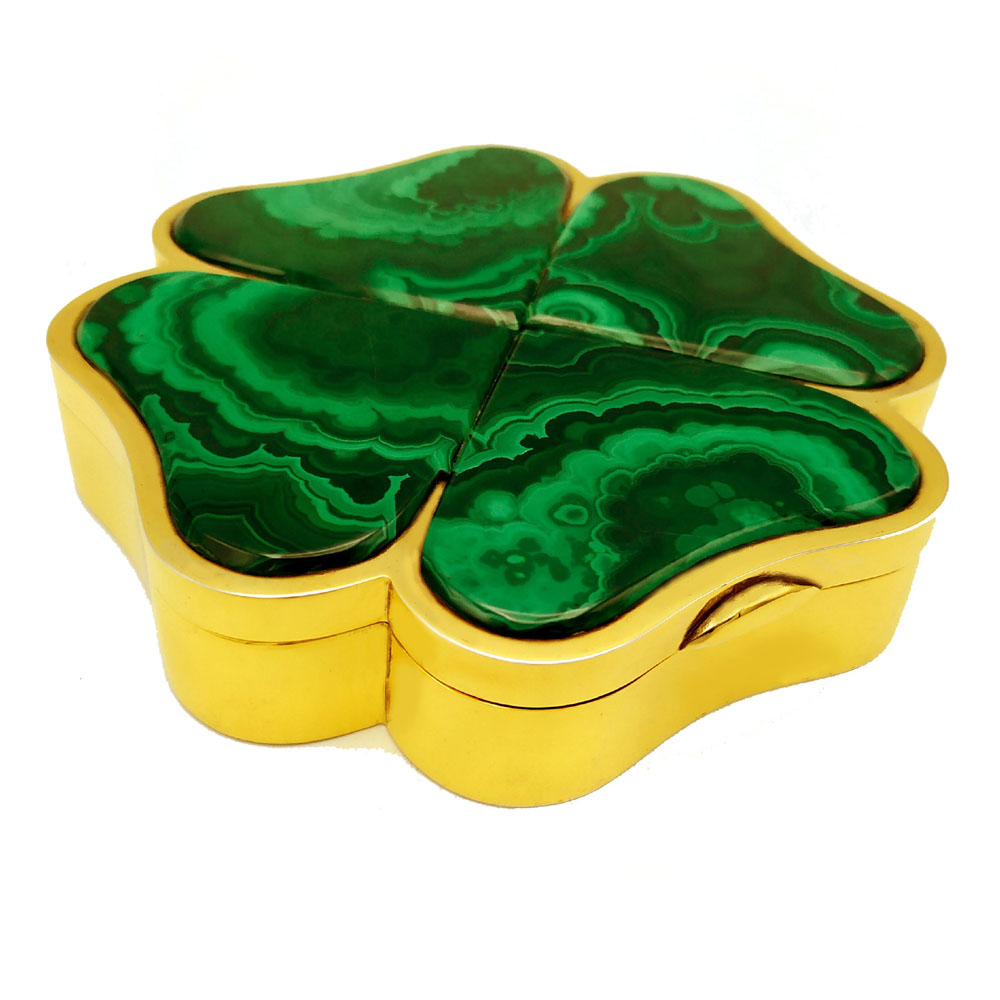 4642-5324 - Table box in the shape of a four-leaf clover in sterling silver 925/1000 gold plated and real malachite stone petals. Dimensions cm. 12 x 12 x 2.5 . Silver weight gr. 340. Designed by Giorgio Salimbeni in 1975 and produced in Florence in several specimens in the Salimbeni company headquarters with manual processing by talented artisan artists also experts in the processing of semi-precious stones and by the "Commesso Fiorentino" of ancient Medici memory (Opificio delle Pietre Dure). Malachite is well known and fascinating: semi-precious stone that has always been it is combined with silver or gold allowing the creation of objects of extreme beauty.