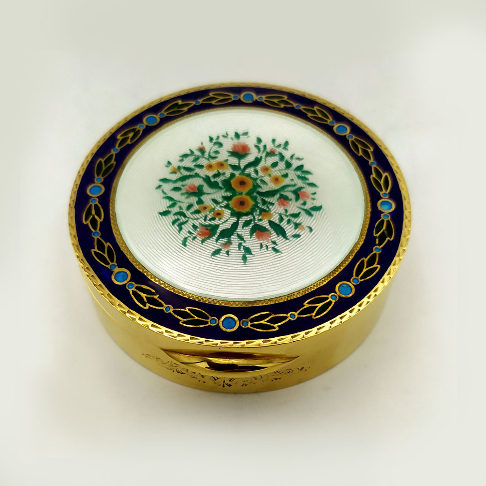 5977-6919 - Round snuff box in 925/1000 sterling silver gold plated with translucent fired enamels on guillochè and hand-painted floral miniature, surrounded by a frame with leaves on a blue background. Art Nouveau style early 1900s. Measure diameter cm. 7.8 high cm. 2.3. Weight gr. 192. Designed by Franco Salimbeni in 1974 and manufactured in numerous specimens with different colors and decorations, in Florence at the headquarters of the Salimbeni Company with completely manual execution by artisan artists with a thick slab and large reinforcements suitable for withstanding numerous enamelled firings at about 750°